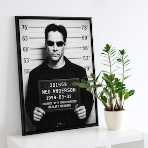 Puede incluir: Impresión enmarcada en blanco y negro con una foto policial de Neo Anderson. La impresión incluye una tabla de altura, el número 301559 y el texto "NEO ANDERSON 1999-03-31 CHARGED WITH UNAUTHORIZED REALITY BENDING."