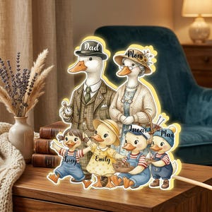 May include: A decorative family of ducks, each with personalized names, in a charming illustration. The duck family includes a father in a suit, a mother in a cardigan, and three children. The artwork is set against a warm, inviting background.