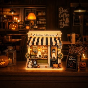 May include: A miniature illuminated coffee shop model named Sophia's Coffee Shop, featuring a black and white striped awning, ghost figurines, miniature coffee equipment, shelves with jars, and Halloween-themed decor including pumpkins.