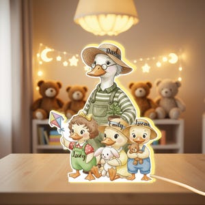 May include: A charming duck family night light, featuring Dad, Emily, Lucy, and Lucas. Each duck wears a hat and holds a toy. The night light sits on a wooden surface, with teddy bears visible in the background, creating a warm, inviting glow.