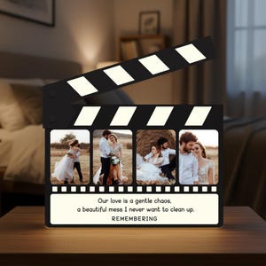 May include: A black clapperboard-shaped photo frame with four picture slots and a white illuminated top. The frame displays wedding photos and the text "Our love is a gentle chaos, a beautiful mess I never want to clean up. REMEMBERING."