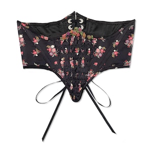 Front flat view of Swiss waist style lingerie underbust corset with multi colored floral print on a black background and gathered front panel with petite ribbon flower detailing in nostalgic cottagecore Victorian style, perfect for romantic pinups.