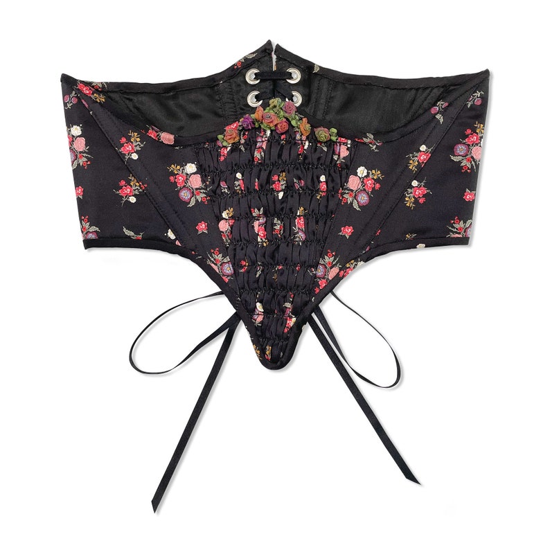 Front flat view of Swiss waist style lingerie underbust corset with multi colored floral print on a black background and gathered front panel with petite ribbon flower detailing in nostalgic cottagecore Victorian style, perfect for romantic pinups.