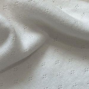 Close up of cotton pointelle fabric in soft knit with tiny diamond motif eyelet pattern in delicate, warm milky white.