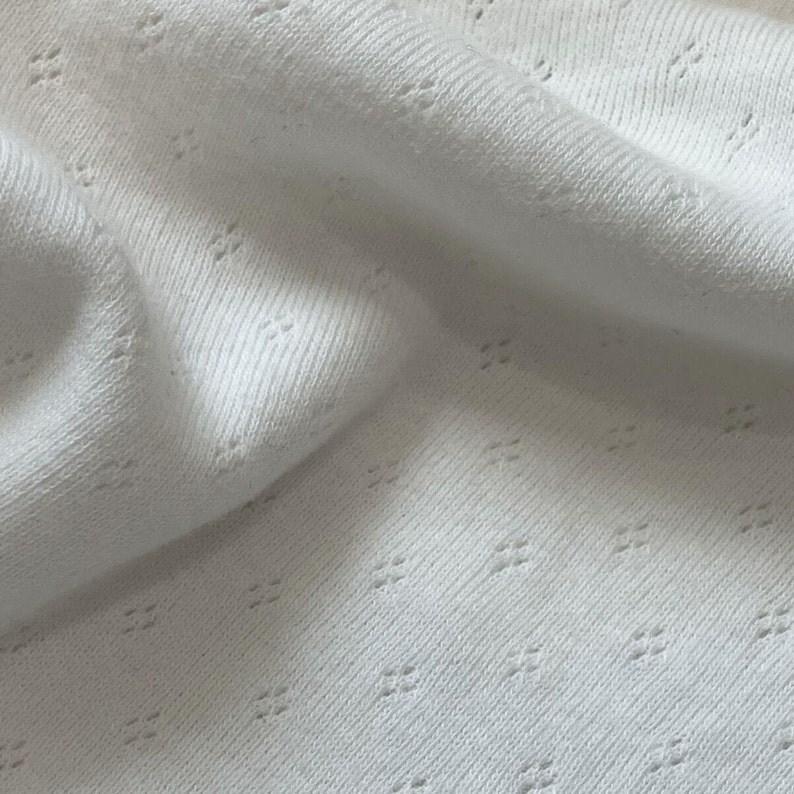 Close up of cotton pointelle fabric in soft knit with tiny diamond motif eyelet pattern in delicate, warm milky white.