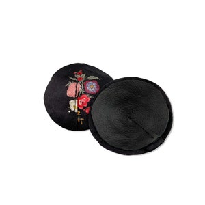 Flat lay of lingerie silk floral pasties in black satin with multi-colored floral bouquet print in circle shape with straight black stitch line. Overturned nipple cover reveals a black leather backing for a luxury, sexy feel.