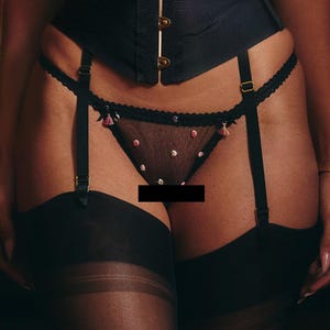 May include: Black lingerie set with a sheer, polka dot panty and garter straps. The panty has delicate pink tassels.