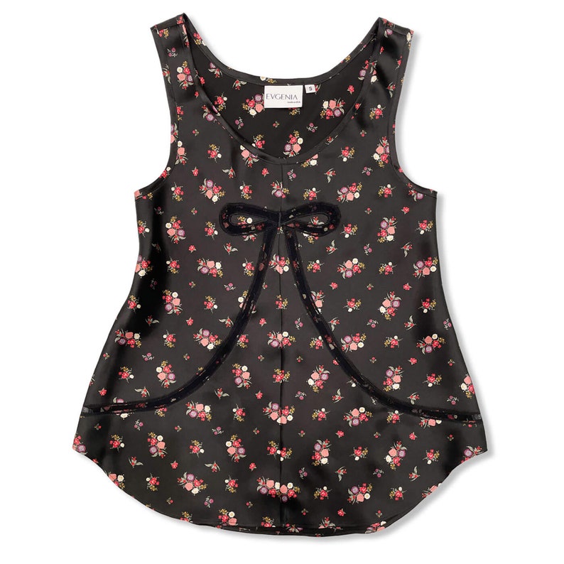 Flat lay of black silk tank top camisole for lingerie wear. Made of silk charmeuse with an antique-inspired floral print on a black background, bias cut for a flattering, body skimming fit. Front panel has a sheer lace bow detail in style of 1920s.