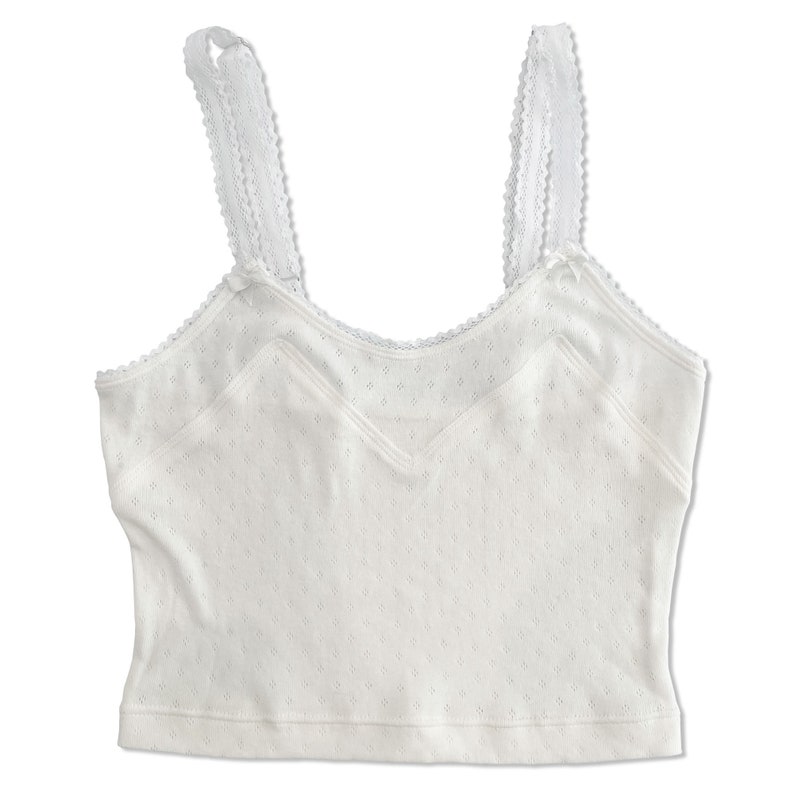 Flat lay of cropped white lingerie camisole top in playful vintage cottagecore style. Cami hits below natural waist and has angular miters to accentuate the bustline with soft picot elastic trim and straps with satin bow details in 1990s Y2K style.