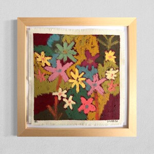 May include: A framed square artwork on textured fabric featuring a vibrant floral pattern with pink, yellow, blue, and white flowers against a deep maroon and olive green background. The bottom right corner displays the handwritten text 01/08/26.