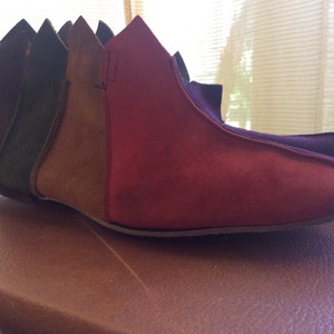 Puede incluir: Un par de botas de punta de color marrón oscuro con paneles de ante de diferentes colores. Los paneles son de color verde, marrón, burdeos y morado.