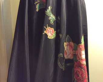 May include: A black skirt with a floral design featuring pink, green, and gold accents. The skirt is made of a silky fabric and has a flowing silhouette.