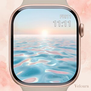 Puede incluir: Un reloj inteligente de oro rosa con una pantalla que muestra una serena escena oceánica al atardecer. La esfera del reloj muestra la hora 11:11 y el día, viernes. La correa del reloj es de color beige claro.