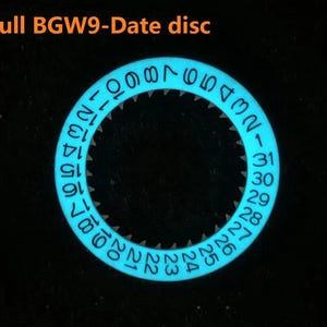 May include: A glowing blue watch date disc with white numerals against a black background. The disc is circular with numbers 1-31 around the edge. The text "Full BGW9-Date disc" is at the top.