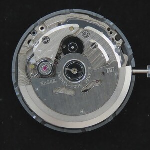 May include: A close-up of a watch movement, showcasing intricate gears, springs, and jewels. The mechanism is primarily silver with a gray outer ring. The text "TWENTY-FOUR JEWELS" and "NH34A" are visible. A silver stem extends from the side.