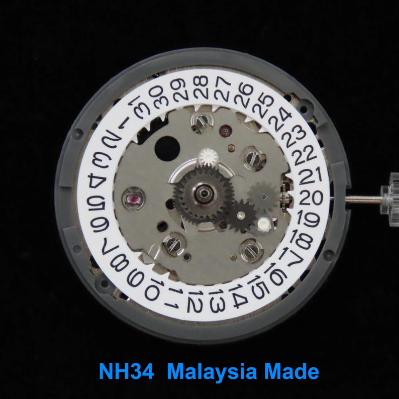 May include: Close-up of a watch movement with a white date ring displaying numbers. The movement has various gears and components, with the text "NH34 Malaysia Made" at the bottom. The watch movement is set against a black background.