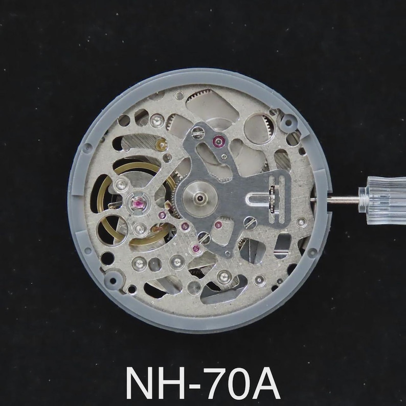 May include: A detailed view of a watch movement, featuring intricate gears, springs, and jewels. The movement is encased in a gray frame, with a clear tool inserted. The text "NH-70A" is displayed at the bottom.