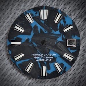 Puede incluir: Una esfera de reloj con un diseño de carbono forjado azul y negro. La esfera presenta marcadores de hora rectangulares blancos y negros y una pantalla digital. El texto "FORGED CARBON 660 ft = 200m AUTOMATIC" está impreso.