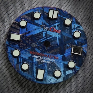 May include: A watch face with a blue abstract design and the text "THE ONE" in red. It features white circular and rectangular markers. The text "METEORMASTER LIMITED EDITION AUTOMATIC" is also visible.