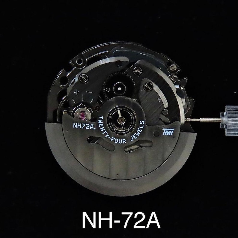 May include: A close-up of a watch movement, featuring intricate gears and components. The movement is primarily black with silver accents, and the text "NH72A" is visible. The words "Twenty-Four Jewels" are also printed on the movement.
