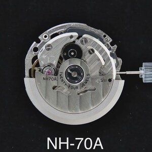 May include: A close-up of a watch movement, featuring intricate gears, springs, and jewels. The silver-toned mechanism is labeled "NH70A" and "Twenty-Four Jewels". A clear plastic stem extends from the side. The overall design is mechanical and detailed.