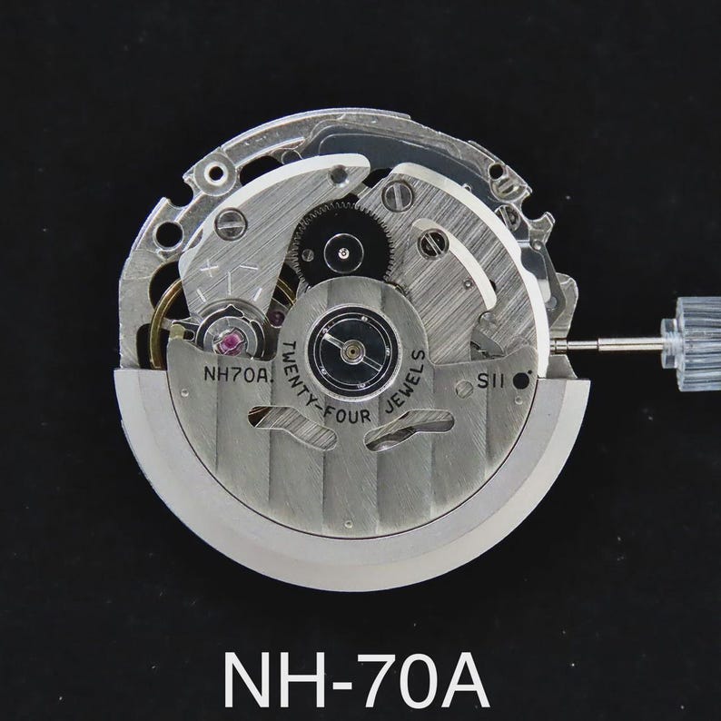 May include: A close-up of a watch movement, featuring intricate gears, springs, and jewels. The silver-toned mechanism is labeled "NH70A" and "Twenty-Four Jewels". A clear plastic stem extends from the side. The overall design is mechanical and detailed.