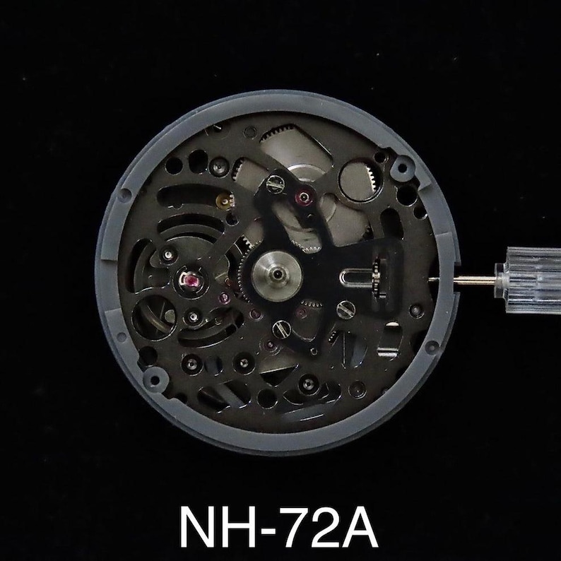 May include: A close-up of a watch movement with intricate gears and components. The watch mechanism is encased in a gray circular frame. The text "NH-72A" is printed at the bottom of the image.