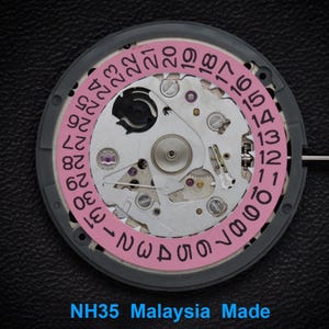 Puede incluir: Primer plano de un movimiento de reloj con una rueda de fecha rosa y engranajes plateados. La rueda de fecha muestra números del 1 al 31. El texto "NH35 Malaysia Made" es visible en la parte inferior.