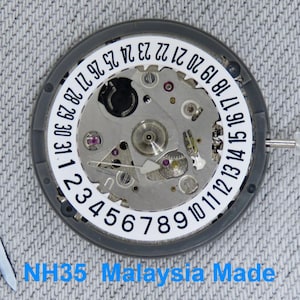 May include: Close-up of a watch movement with a white date dial and silver gears. The dial displays numbers 1-31. The text "NH35 Malaysia Made" is visible at the bottom. The watch movement is set against a gray background.