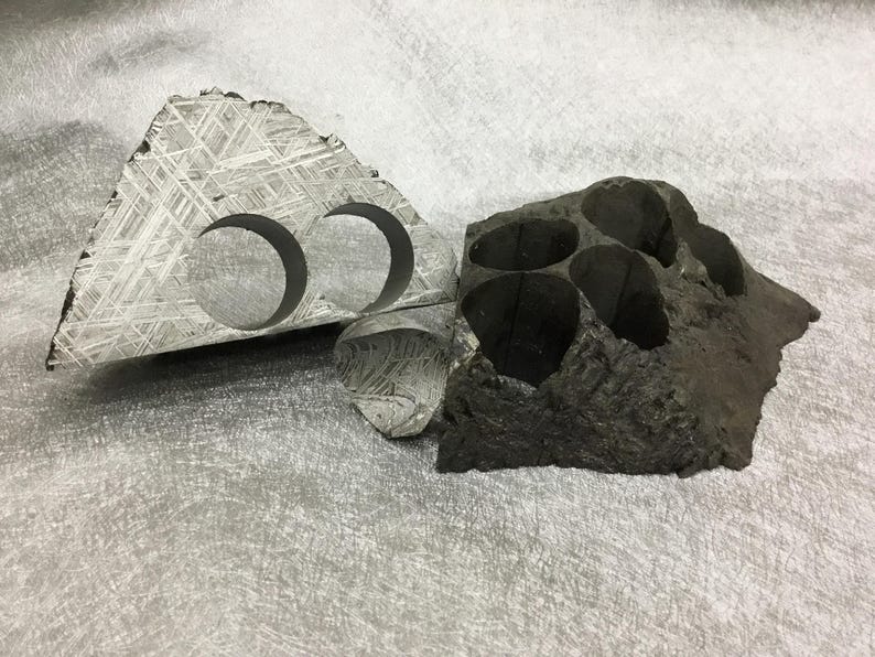 May include: Two pieces of textured, gray stone. One is triangular with two circular cutouts. The other is a dark, irregular shape with multiple openings. The stone has a unique, cross-hatched pattern.