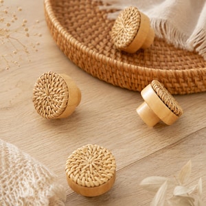 Può includere: Un set di quattro pomelli rotondi per mobili con base in legno marrone chiaro e inserto circolare superiore in rattan naturale intrecciato. Ogni pomello presenta un corpo cilindrico liscio e una superficie in rattan testurizzato con motivo radiale.