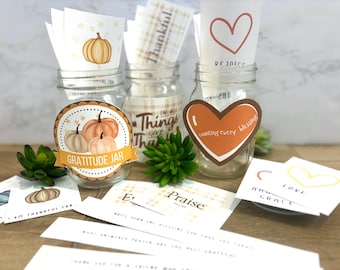 Könnte beinhalten: Drei transparente Gläser mit dekorativen Etiketten und Karten. Ein Glas hat ein Etikett mit der Aufschrift "Gratitude Jar" mit Kürbisillustrationen. Andere Gläser haben Karten mit Herzen und den Worten "Thankful" und "counting every blessing".