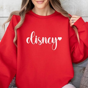 May include: A red sweatshirt with the word "Disney" in white script, with a small heart symbol. The sweatshirt is a solid color and has a crew neck. The sleeves are long and the material appears to be soft.