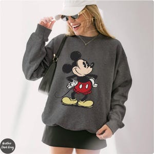Pode incluir: Camisola cinza escuro com um desenho do Mickey Mouse. A personagem de desenho animado usa cal&ccedil;&otilde;es vermelhos, sapatos amarelos e luvas brancas. A camisola tem mangas compridas e gola redonda. O texto "Heather Dark Gray" &eacute; vis&iacute;vel.