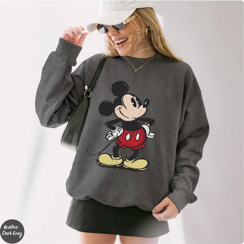 Pode incluir: Camisola cinza escuro com um desenho do Mickey Mouse. A personagem de desenho animado usa cal&ccedil;&otilde;es vermelhos, sapatos amarelos e luvas brancas. A camisola tem mangas compridas e gola redonda. O texto "Heather Dark Gray" &eacute; vis&iacute;vel.