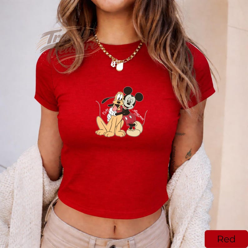 Puede incluir: Un top corto rojo con un gr&aacute;fico de Mickey Mouse y Pluto abraz&aacute;ndose. Los personajes de dibujos animados est&aacute;n representados en un abrazo amistoso, con Mickey con su atuendo ic&oacute;nico y Pluto sentado. La parte superior es de color rojo brillante.