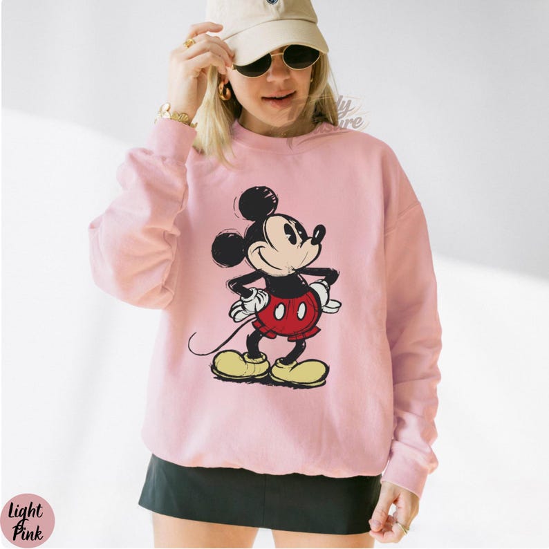 Pode incluir: Camisola rosa claro com um desenho do Mickey Mouse. A personagem de desenho animado &eacute; em preto, vermelho, amarelo e branco. A camisola tem mangas compridas e gola redonda. A imagem &eacute; uma ilustra&ccedil;&atilde;o em estilo vintage.