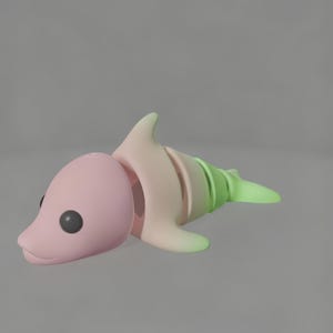 May include: A segmented dolphin figurine in pastel colours. The head and body are pink, fading to a light green tail. The dolphin has black eyes and a smooth, rounded form, ideal for a child's toy.