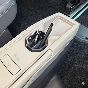 Könnte beinhalten: Beige Autokonsole mit eingebautem Staufach. Im Fach befinden sich ein schwarzer Stift, Schlüssel und eine Karte. Ein Knopf mit der Aufschrift "PUSH" ist auf der Konsole sichtbar.