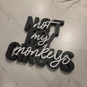 May include: A black and white wooden sign that reads "NOT MY CIRCUS" in a combination of bold, block letters and elegant cursive script. The sign is a decorative item.