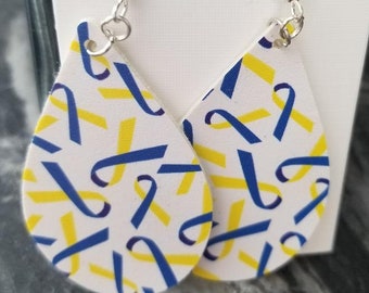 Puede incluir: Un par de pendientes colgantes con fondo blanco y un patrón de cintas azules y amarillas. Los pendientes están hechos de cuero y tienen ganchos plateados.