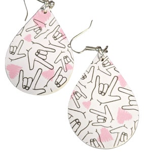 Könnte beinhalten: Ein Paar weiße tropfenförmige Ohrringe mit einem pinkfarbenen und schwarzen Handgestenmuster. Die Ohrringe haben silberne Haken.