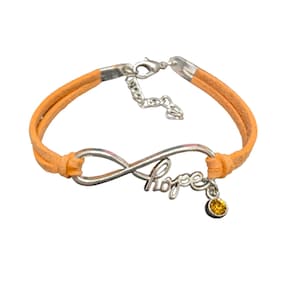 Puede incluir: Pulsera de cuero naranja con un dije de símbolo de infinito y la palabra "esperanza" inscrita en él. Un pequeño cristal amarillo cuelga del dije.