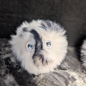 May include: A white and black fluffy ball with googly eyes. The ball is made of soft, plush material and has a black and white pattern.