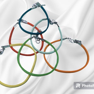 Puede incluir: Colección de seis pulseras coloridas. Cada pulsera presenta un cordón fino y redondo en diferentes colores: amarillo, verde, naranja, azul claro, azul oscuro y rojo. Las pulseras tienen cierres plateados.