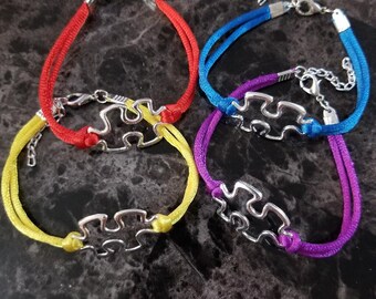 May include: Four colorful friendship bracelets with silver puzzle piece charms. The bracelets are red, yellow, blue, and purple.