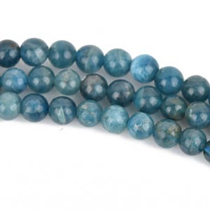 May include: A strand of blue apatite beads. The beads are round and smooth, with a slightly translucent appearance.