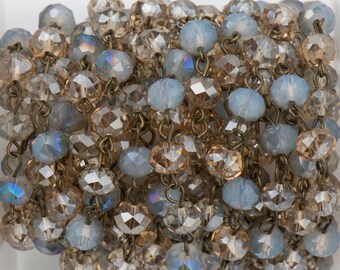May include: A strand of crystal beads in shades of light blue and brown, strung on a silver chain. The beads are faceted and have a shimmering effect.