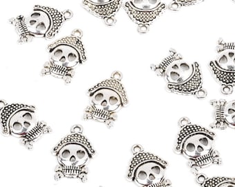 May include: Silver-toned metal skull charms with a hat and crossbones. These small charms are ideal for jewelry making or crafting projects. The charms are scattered on a white background.