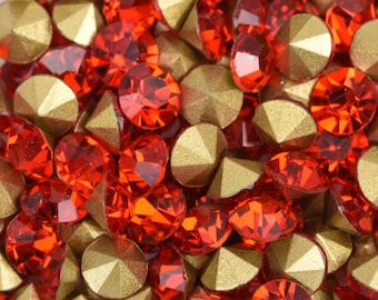 May include: A collection of red and gold rhinestones. The red rhinestones have a faceted, jewel-like appearance, while the gold ones have a metallic, matte finish. The rhinestones are in various shapes, including round and pointed.